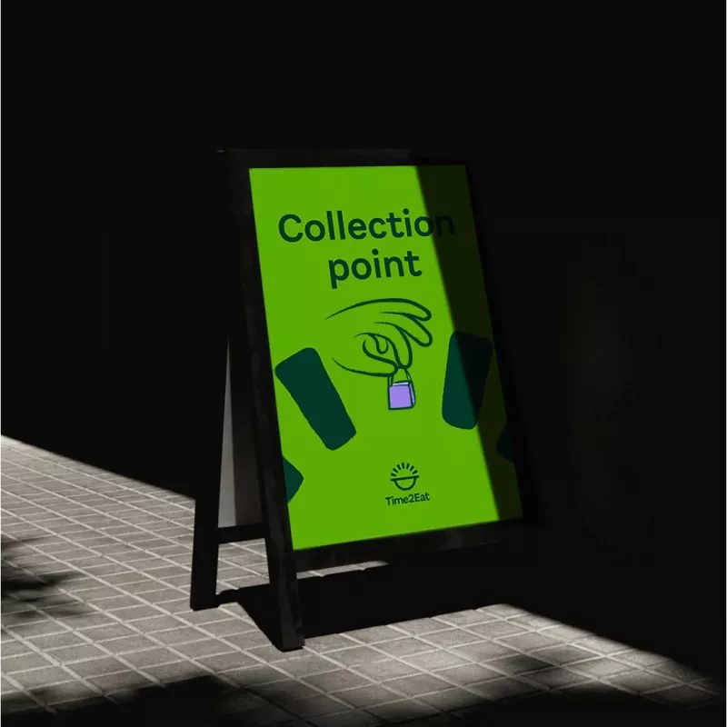 A board sign outside of restaurant / office . Written on it large 'Collection Point' with illustrated hand holding a mini shopping bag
